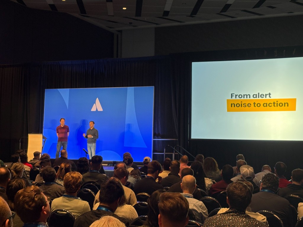 Dushyant Sharma and Rick Westbrock on stage at Atlassian Team ’26 with the “From alert noise to action” title slide.